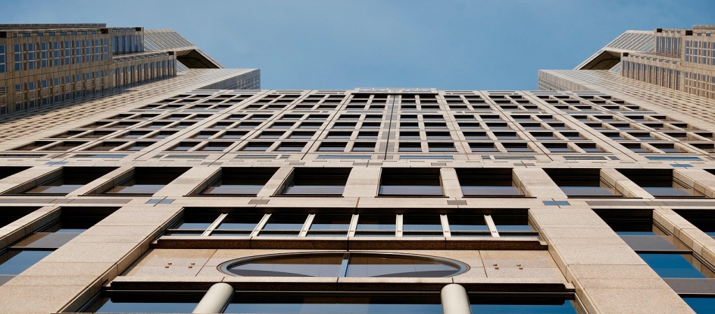 A tall American skyscraper pulled upward from the base, symbolizing instability during the 2025 U.S. government shutdown and its impact on immigration.