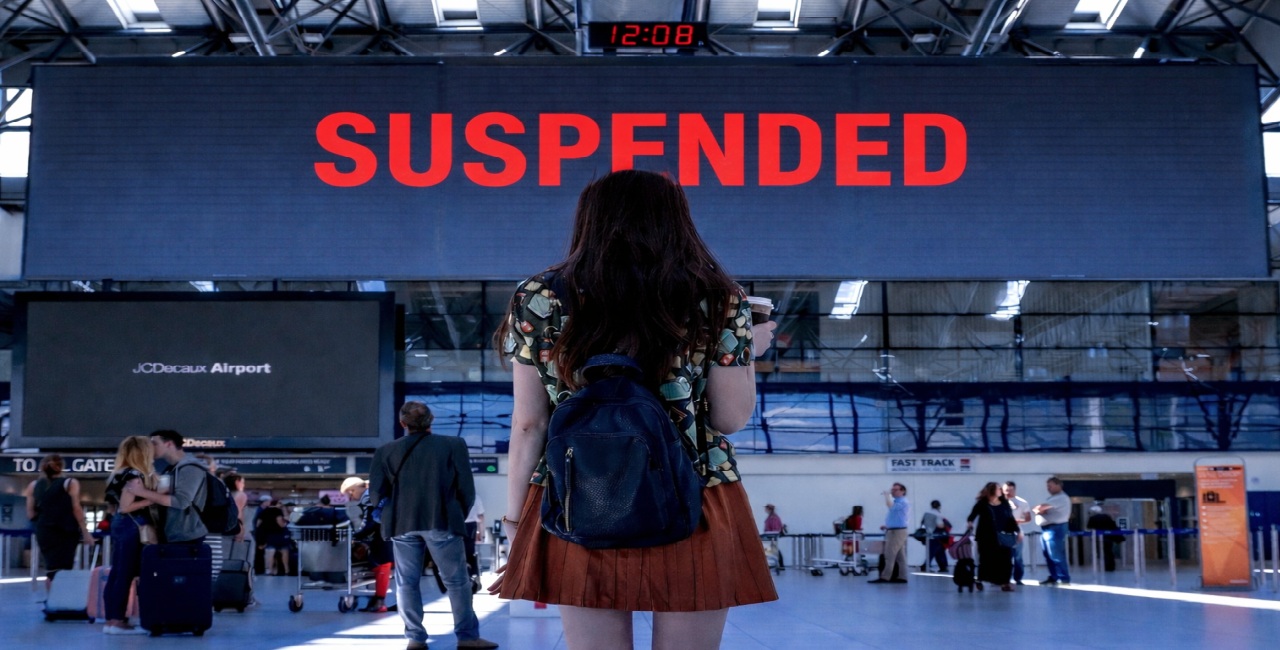Havalimanında “SUSPENDED” yazılı ekrana bakan yolcu; göçmen vizeleri sürecindeki kısıtlamaları simgeliyor.